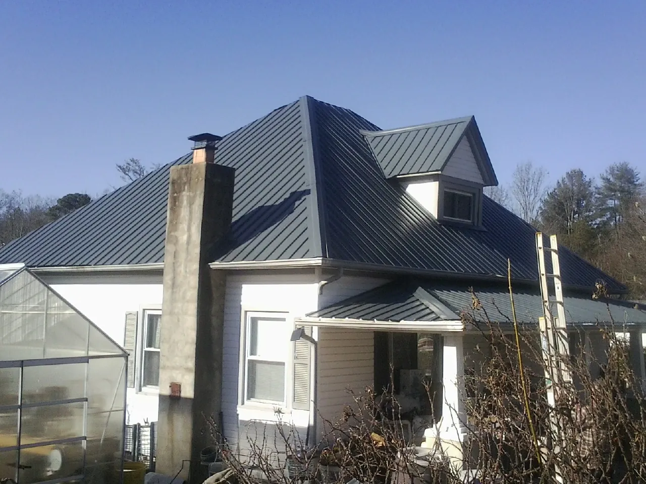 Dark blue standing seam metal roof on a white farmhouse with dormer — Slate & Tile Roof Repair by Roofing Brothers in Kenedy