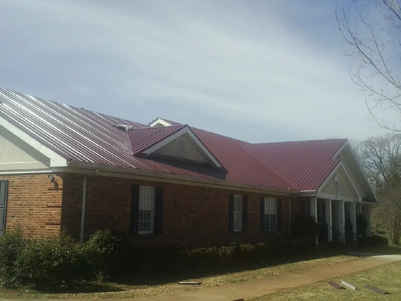 Red metal roof with gabled entries on a long brick building, from a Hail Damage Roof Repair job in Kenedy
