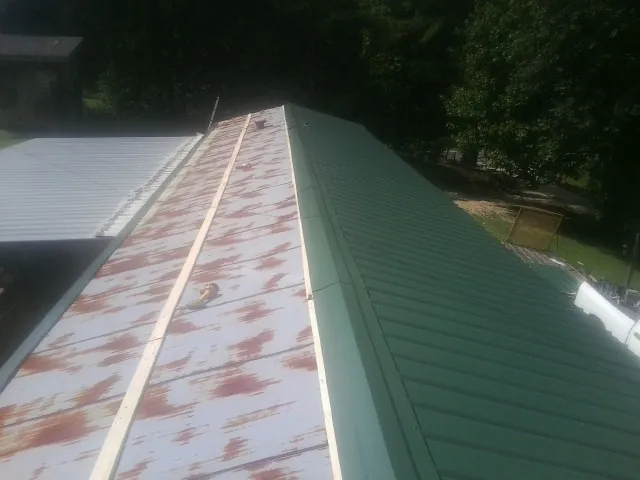 Old rusted panels beside newly installed green metal roofing — Wind Damage Roof Repair by Roofing Brothers in Kenedy