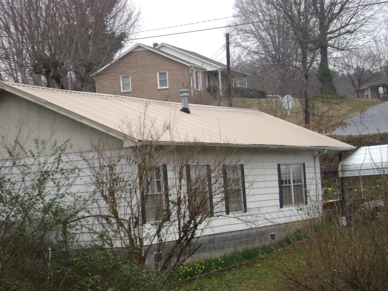 Tan metal roof on a white sided house set into a hillside — Commercial Roofing by Roofing Brothers in Kenedy