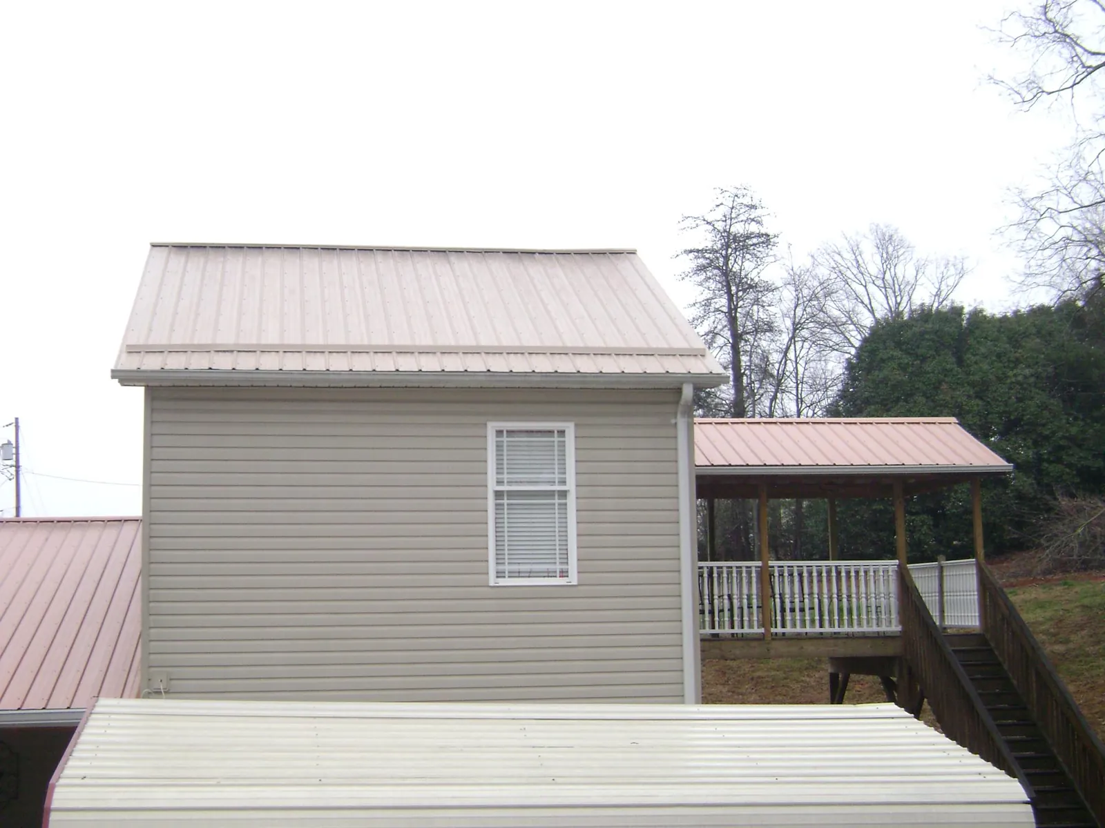 Tan metal roofs on a two story addition and attached porch, from a Roof Replacement job in Kenedy